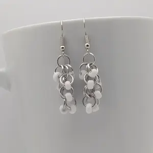 Bright silver aluminum chain mail earrings with white beads on a white mug.