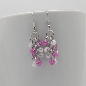 Bright silver aluminum chain mail earrings with white and rose beads on a white mug.