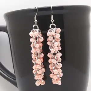 Bright silver aluminum long chain mail earrings with coral beads on a black mug.