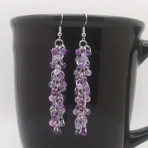 Bright silver aluminum long chain mail earrings with violet mix beads on a black mug.