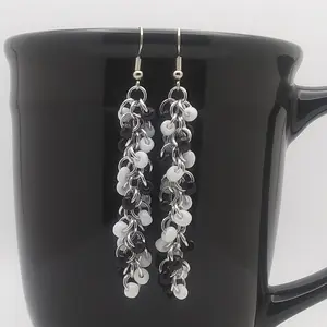 Bright silver aluminum long chain mail earrings with black and white beads on a black mug.