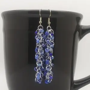 Bright silver aluminum long chain mail earrings with sapphire mix beads on a black mug.