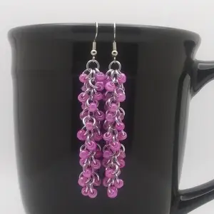 Bright silver aluminum long chain mail earrings with rose beads on a black mug.