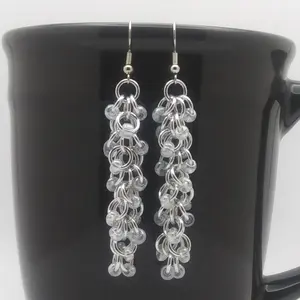 Bright silver aluminum long chain mail earrings with crystal luster beads on a black mug.