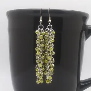 Bright silver aluminum long chain mail earrings with yellow luster beads on a black mug.