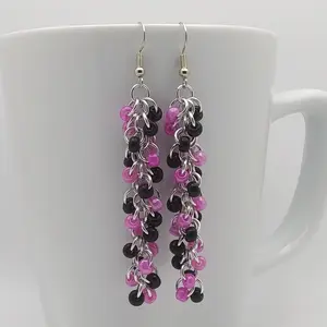 Bright silver aluminum long chain mail earrings with black and rose beads on a white mug.