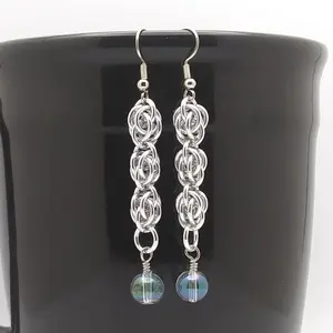 Bright silver aluminum chain mail earrings with green ab glass round beads on a black mug.