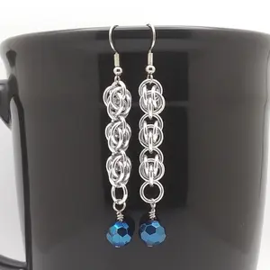 Bright silver aluminum chain mail earrings with metallic blue faceted glass beads on a black mug.