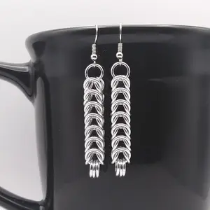 Bright silver aluminum chain mail earrings on a black mug.