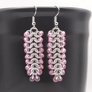 Bright silver aluminum chain mail earrings with pink luster beads on a black mug.