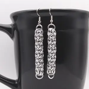 Bright silver aluminum chain mail earrings on a black mug.