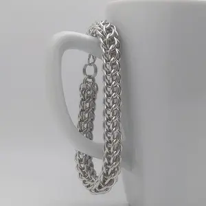 Bright silver aluminum chain mail bracelet on a white mug.