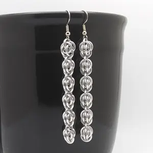 Bright silver aluminum chain mail earrings on a black mug.